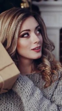 Kadın hediye kutularını açıyor. Yeni yılda hediyeleri olan genç bir kadın oturma odasında dikey videoda.