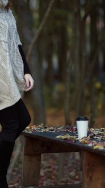 Bir kadın parkta vakit geçiriyor. Genç bir kadın sonbahar parkında bir fincan kahveyle vakit geçiriyor.