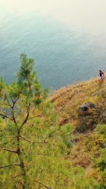 Denize yakın bir tepede yürüyen genç bir çiftin kuş bakışı görüntüsü. Aşık erkek ve kadın güneşli bir yaz gününde doğada yürürler. Hava görüntüsü. Dikey video