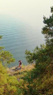 Deniz kıyısında birbirine sarılan romantik bir çift. Güneşli yaz gününün doğal manzarası ve genç bir adamla bir kız öpüşüyor. Hava görüntüsü. Dikey video