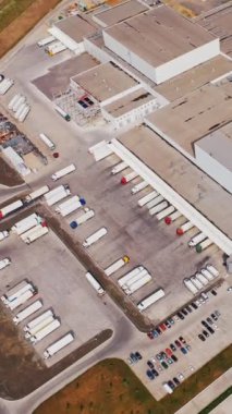 Birçok kamyonun ticaret mallarını yükleyip indirdiği Endüstriyel Depo Binası / Yükleme Alanının Hava Çekimi. Dikey video