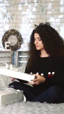 Kadın hediye kutularını açıyor. Yeni yılda hediyeleri olan genç bir kadın oturma odasında dikey videoda.