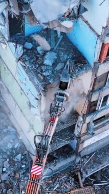 Demolishing vehicle breaks and throws down the parts of ruined house. Dismantling the old building with the help of machinery. View from above. Vertical video
