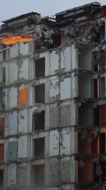 Collapse of the ruined roofs of an old house. Excavator grabber tears off the pieces of the roof. Blue sky at the backdrop. Vertical video