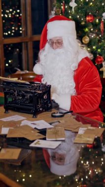 Noel Baba evinde tatil mektupları yazıyor. Noel süsleri, hediyeler ve masada oturan Noel Baba şöminenin arkasındaki daktiloda çalışıyor. Dikey video