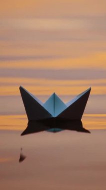 Origami teknesi akşam su yüzeyinde. Beyaz kağıttan tekne gölgesi suda yüzer. Yakın plan. Dikey video