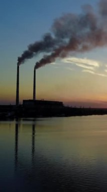 Nehir Üzerindeki Güç İstasyonu. Sunaset Dikey Video 'da nehire duman döken boruları olan elektrik santrali.