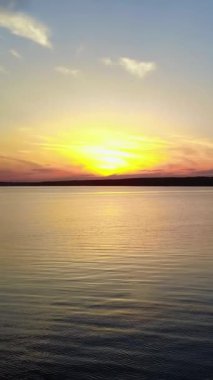 Gün batımında Nehir kenarındaki Gençler. Gün batımında nehir suyunda seyreden gençlerin siluetleri. Dikey video.