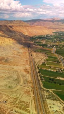 Arabalar güzel kanyon dağlarının eteklerindeki otoyolda hızla ilerliyorlar. Colorado, ABD 'deki muazzam kayaların yakınında bir sürü yeşillik bulunan bir kasaba. Üst Manzara. Dikey video