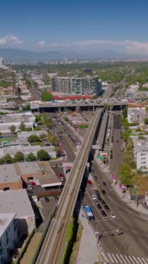 Los Angeles, Kaliforniya 'nın şehir bölgesinde alçak binalar. Kalabalık yollar, birden fazla arabanın hızla geçmesiyle kenti geçiyor. Güneşli gün görüntüleri. Üst Manzara. Dikey video