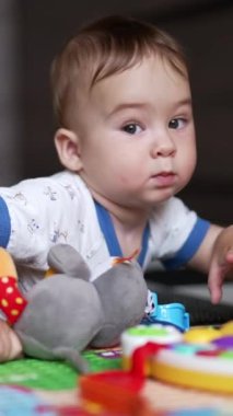 Yerde yatıp oyuncaklarına daha yakın sürünen tatlı küçük çocuk. Güzel çocuk diğer oyuncaklar arasından araba seçiyor. Kapatın. Dikey video