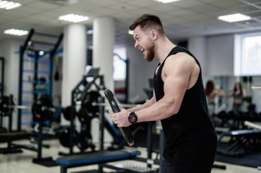 Siyah kolsuz tişörtlü bir adam elinde bir ağırlık tutuyor ve kızgın görünüyor.