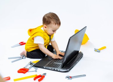 Bir bebek yerde oturuyor ve dizüstü bilgisayarda yazıyor. Laptop açık ve siyah bir klavyesi var..