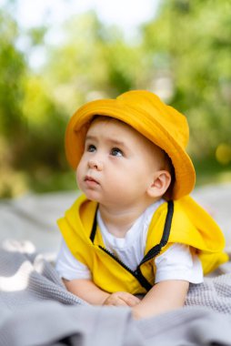 Sarı şapkalı ve sarı ceketli bir bebek battaniyenin üzerinde yatıyor. Bebeğin yüzünde tuhaf bir ifade var.