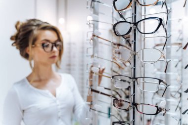 Bir kadın gözlük ekranına bakıyor. O da gözlük takıyor. Ekranın birçok farklı şekil ve renk gözlükleri var.