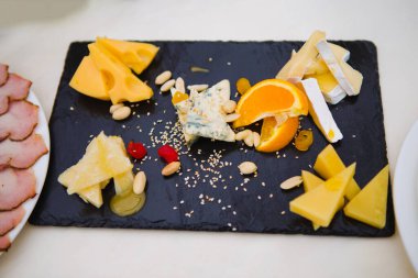 Üzerinde çeşitli peynirler ve meyveler olan siyah bir tepsi. Peynirler arasında mavi peynir, keçi peyniri ve beyaz peynir var..