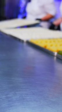 Aşçılar tepsileri hazır hamur işiyle sergiliyorlar. Fabrika işçileri doldurulmuş krepleri metal masaya koydu. Arkaplan bulanık. Dikey video