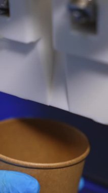 Mavi eldivenlerle yemek otomatının altına kağıt bardak koyuyorlar. Yumuşak kremalı dondurma bardağı yakından dolduruyor. Dikey video