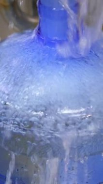 Büyük şişe çabucak tatlı suyla doldurulur. Dolu şişe konveyör tarafından taşınıyor. Kapatın. Yiyecek fabrikası konsepti. Dikey video