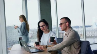 Ofis çalışanları kahve içer ve iş konularını dizüstü bilgisayarla tartışırlar. Arka plandaki kadın telefonunu kullanıyor. .