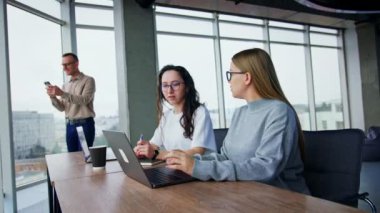 İşle ilgili konuları konuşmakla meşgul kadınlar. Arka plandaki adamın telefonunda görüntülü konuşma var. Düşük açı görünümü.