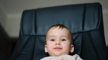 Güzel neşeli çocuk kameraya dilini gösteriyor. Çocuk siyah sandalyede oturuyor ve kameraya bakıyor. Kapat..