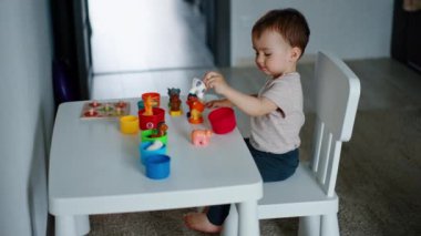 Güzel çocuk küçük masada oturup oyuncaklarla oynuyor. Bebek hayvanları ve renkleri inceliyor.