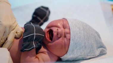 Şapkalı ve eldivenli yeni doğmuş bebek acı acı bağırıyor. Sıhhiyeci çocuğun bezini bağlıyor. Kapat..