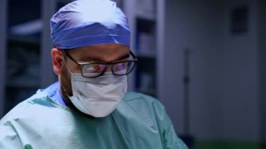 Erkek sakallı, orta yaşlı doktor ameliyathanede çalışıyor. Çalışmaya odaklanmış bir cerrahın yakın plan portresi..