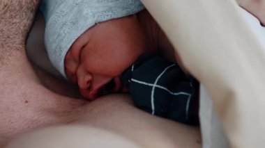 Minik bebek babasının göğsünde yatarken ağlıyor. Bebek doğduktan sonra ilk kez gözlerini açar. Kapat..