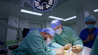 Bir cerrah metal aletlerle cerrahi bölümünü genişletiyor. Ana cerrah bölgeyi işletmek için aletler kullanır. Anestezi uzmanı doktora hitap eden ameliyat masasına yaklaşır..