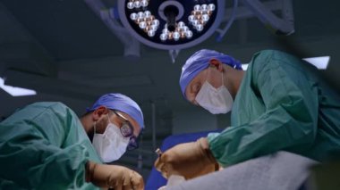 Cerrahi uzmanları bir hastanın iki tarafında yer alır. Yoğunlaşmış doktorlar ameliyat yaparlar. Düşük açı görünümü.