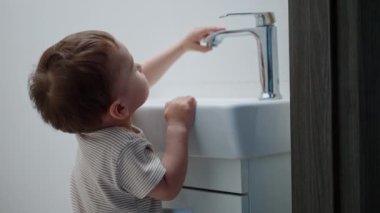 Tatlı çocuk musluğa dokunup batıyor. Bebek suyu açar ve heyecanla akışını izler..