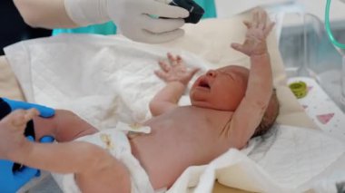 Minik yeni doğmuş bebek sıhhiyeler tarafından soyuluyor. Çocuk mutsuz ve el sallayarak ağlıyor. Kapat..