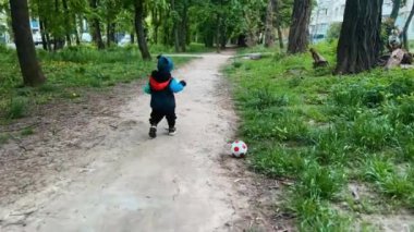 Küçük çocuk baharda parkta bir topla oynuyordu. Kalın elbiseli bebek topu kaldırmak istiyor ama sonra sopanın üzerinde dikkatini dağıtıyor..