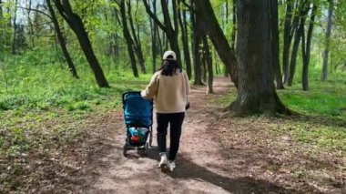 Anneyi bebek arabasıyla takip etmek. Kadın kameraya dönüyor. Anne ve çocuk parkta yürüyüşe çıkıyorlar..