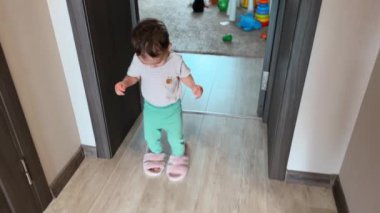 Mutlu çocuk annesinin terliklerini giydi ve odanın etrafında yürüdü. Sevimli çocuk evde oynuyor. Üst görünüm.
