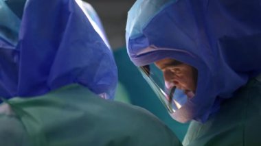 Koruyucu kask takan erkek doktor hastaya bakıyor. Cerrah ameliyat ekibinde işbirliği yapıyor..