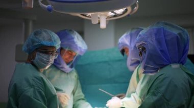 Koruyucu giysiler içindeki cerrahi ekip ameliyathanedeki parlak lambanın altında çalışıyor. Bacak ameliyatında tıbbi profesyonel işbirliği.