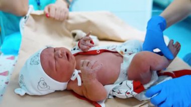 Doktorun eldivenli elleriyle ağlayan yeni doğmuş bir bebek. Doktor masasındaki küçük çocuk. Kapat..