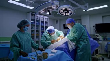 Ana cerrah ayak cerrahisinde metal enstrüman kullanıyor. Doktora yardım etmek ameliyat ayağını tutar. Kadın hemşire elinde aletlerle masada duruyor..