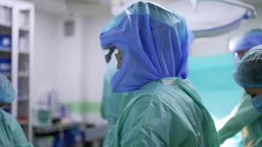 Ameliyattan önce doktorun giyinmesine yardım eden hemşireler. Bir doktor kemeri bağlar, diğeri eldivenleri hazırlar..