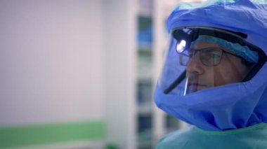 Gözlüklü, farlı ve koruyucu başlıklı özenli bir doktor gözlerinin önünde duruyor. Doktor ameliyattan önce bir hastanın röntgen taramasını inceliyor..