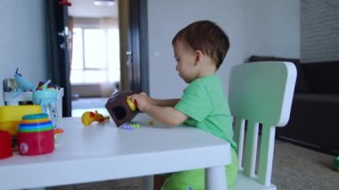 Masada oturan sevimli küçük bir çocuk. Çocuk odada oyuncaklarla oynuyor. Yan görünüm.