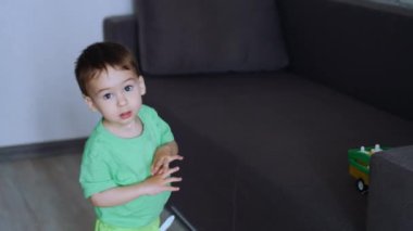 Küçük çocuk kanepeye koşar ve oyuncağını alır. Çocuk bir arabayı koridora götürür ve yere bırakır..