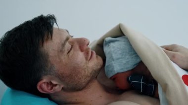Beyaz bir baba yeni doğmuş çocuğunu kucağına aldığı için mutlu. Cilt teması için bebek babasının göğsüne konur..
