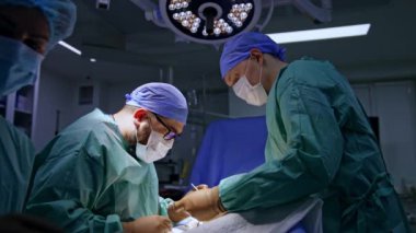 Metal aletlerle hastaya odaklanmış baş cerrah. Doktora yardım etmek, meslektaşına yardım etmek için gerekli aracı tutuyor..