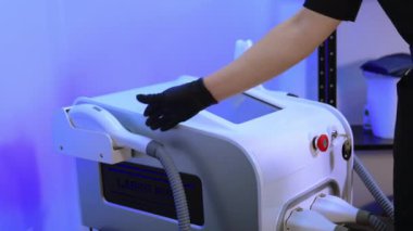Epilasyon uzmanı modern ekipmanların aparatını alır. Kozmetik uzmanı lazeri kontrol eder ve ışık parıltısı görünür..