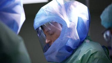 Koruyucu miğferli doktor ameliyat alanına dikkatlice bakıyor. Çalışırken bir cerrahın portresi.