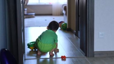 Evde oyuncağıyla oynayan bir çocuğun arka görüntüsü. Çocuk arabasını yere koyar ve gidişini izler..